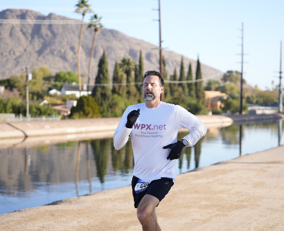 The founder mid-stride on a canal path with desert mountains behind him